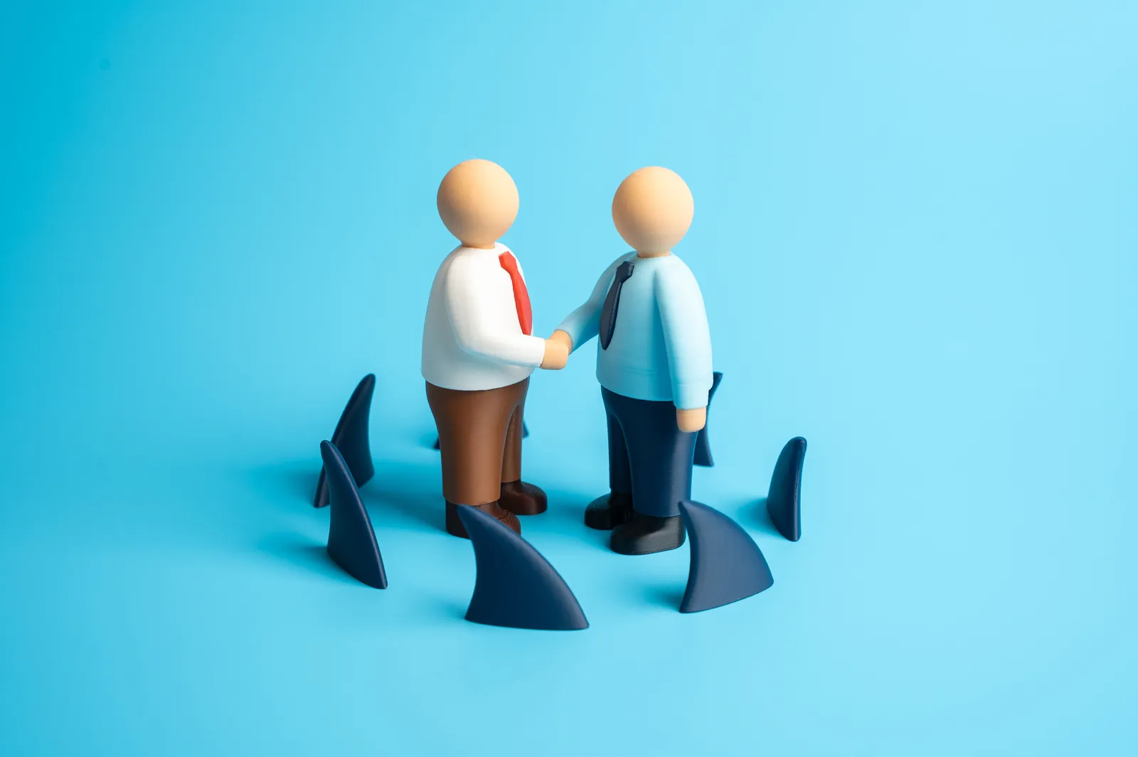 Deux figurines se serrent la main entourées d’ailerons de requins : la confiance à l’épreuve de la fraude.